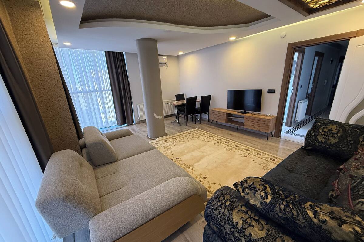 Ett modernt vardagsrum med en soffa, en mönstrad fåtölj, en tv och en matplats med stolar och ett bord.