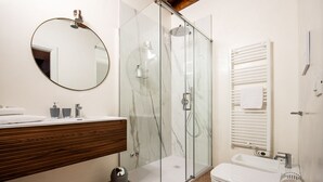 Et moderne badeværelse med et glasbadeværelse, en trækommode, et rundt spejl og toilet med håndklædestang.