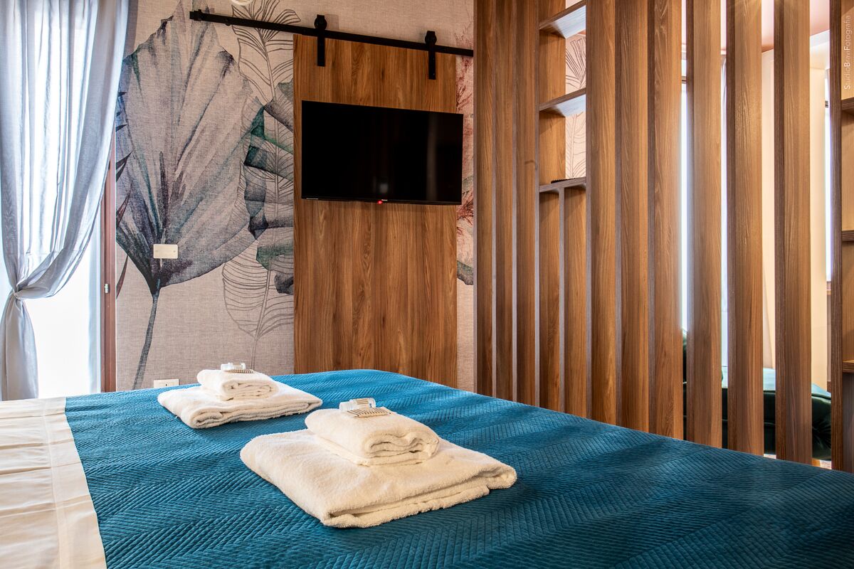 Una habitación de hotel con una cama, un televisor de pantalla plana montado en una pared de madera y un gran mural con motivos de hojas.