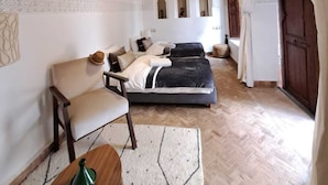 A room with two beds, a chair, a small table, and a large window with curtains. - Dar S'bah (Fes)