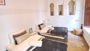 A room with two beds, a wooden ceiling, and a wall with three arched windows. - Dar S'bah (Fes)