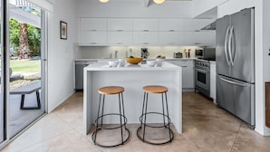 A modern kitchen with white cabinets, a stainless steel refrigerator, two stools, and a breakfast bar. - Racquet Club Rendezvous – Palm Springs Escape (Palm Springs)