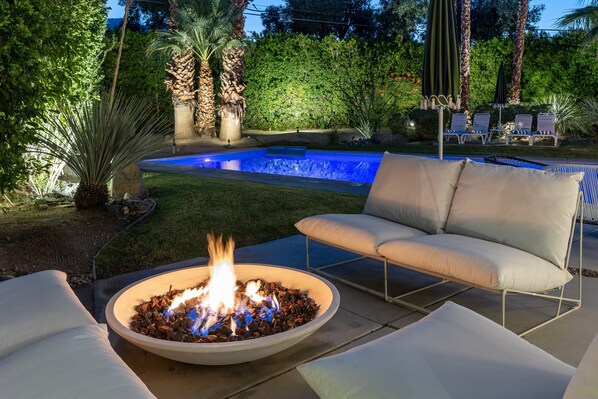 A backyard with a swimming pool, a fire pit, and outdoor seating.