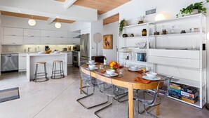 A modern kitchen with white cabinetry, a wooden island, and a dining area with clear chairs and a wooden table. - Racquet Club Rendezvous – Palm Springs Escape (Palm Springs)