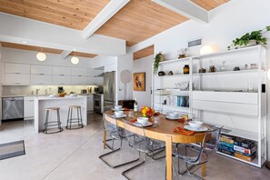 A modern kitchen with white cabinetry, a wooden island, and a dining area with clear chairs and a wooden table. - Racquet Club Rendezvous – Palm Springs Escape (Palm Springs)