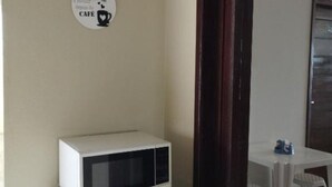 A kitchenette with a microwave and a small refrigerator. There is a wall-mounted sign with a coffee cup and heart symbol. A dining area with a white table and plastic chairs is visible in the background. - Pousada Terra Bela (Buriticupu)
