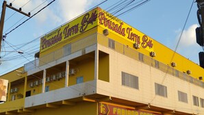 A building with a yellow facade, a sign for 'Pousada Terra Bela', and a construction company sign. - Pousada Terra Bela (Buriticupu)