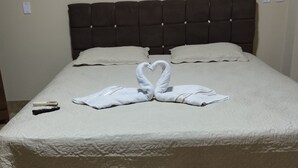 A neatly made bed with a heart-shaped towel arrangement, a remote control, and a fluffy rug. - Pousada Terra Bela (Buriticupu)
