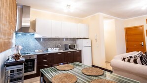 A compact kitchen with dark cabinets, a microwave, and a refrigerator. There is a dining table with woven placemats and a sofa in the adjacent living area. - Céntrico Apartamento en Santa Cruz (Santa Cruz de Tenerife)