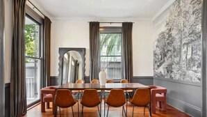 Ein Esszimmer mit einem Holztisch, sechs Stühlen und einem großen Fenster mit Vorhängen.