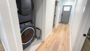 Una lavanderia con lavatrice e asciugatrice affiancate, pavimento in legno e un corridoio che porta a una porta.