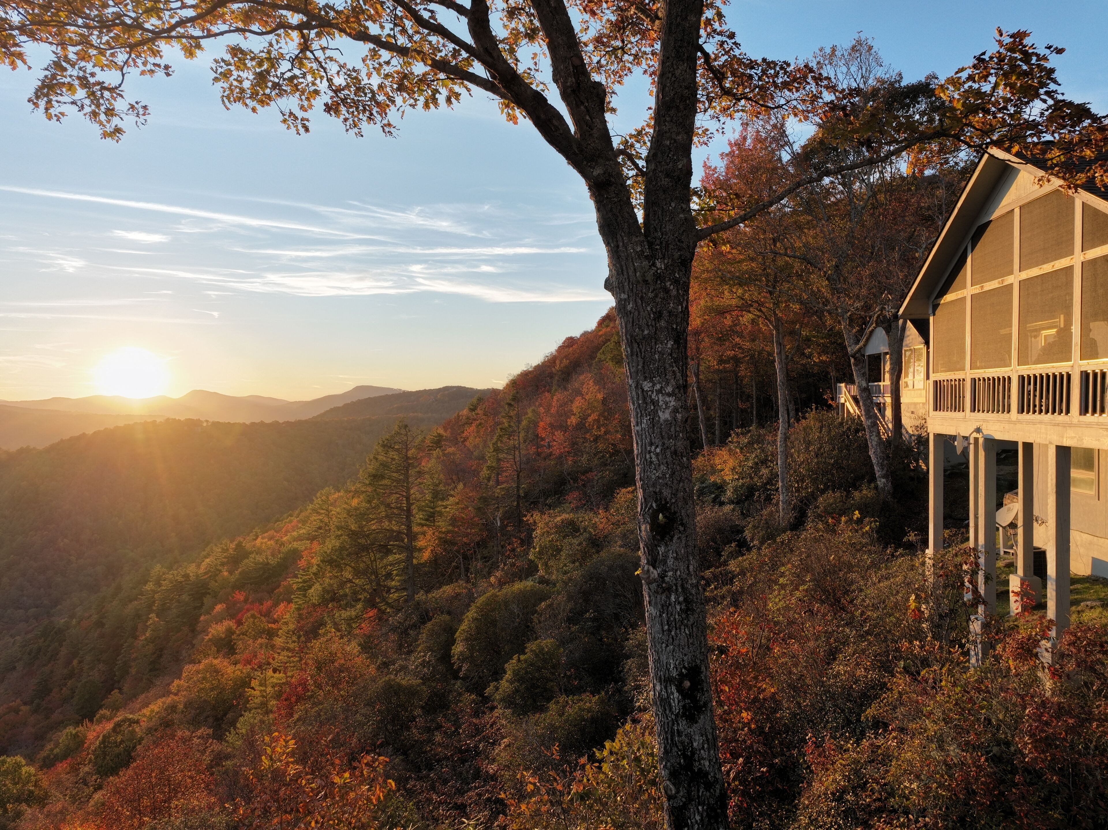 Een chalet met een groot raam dat uitkijkt over een bebost berglandschap tijdens de zonsondergang.
