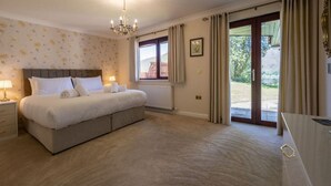 Ein geräumiges Schlafzimmer mit einem großen Bett, einer Chandelüster, einem Fenster mit Vorhängen und Blick ins Freie.