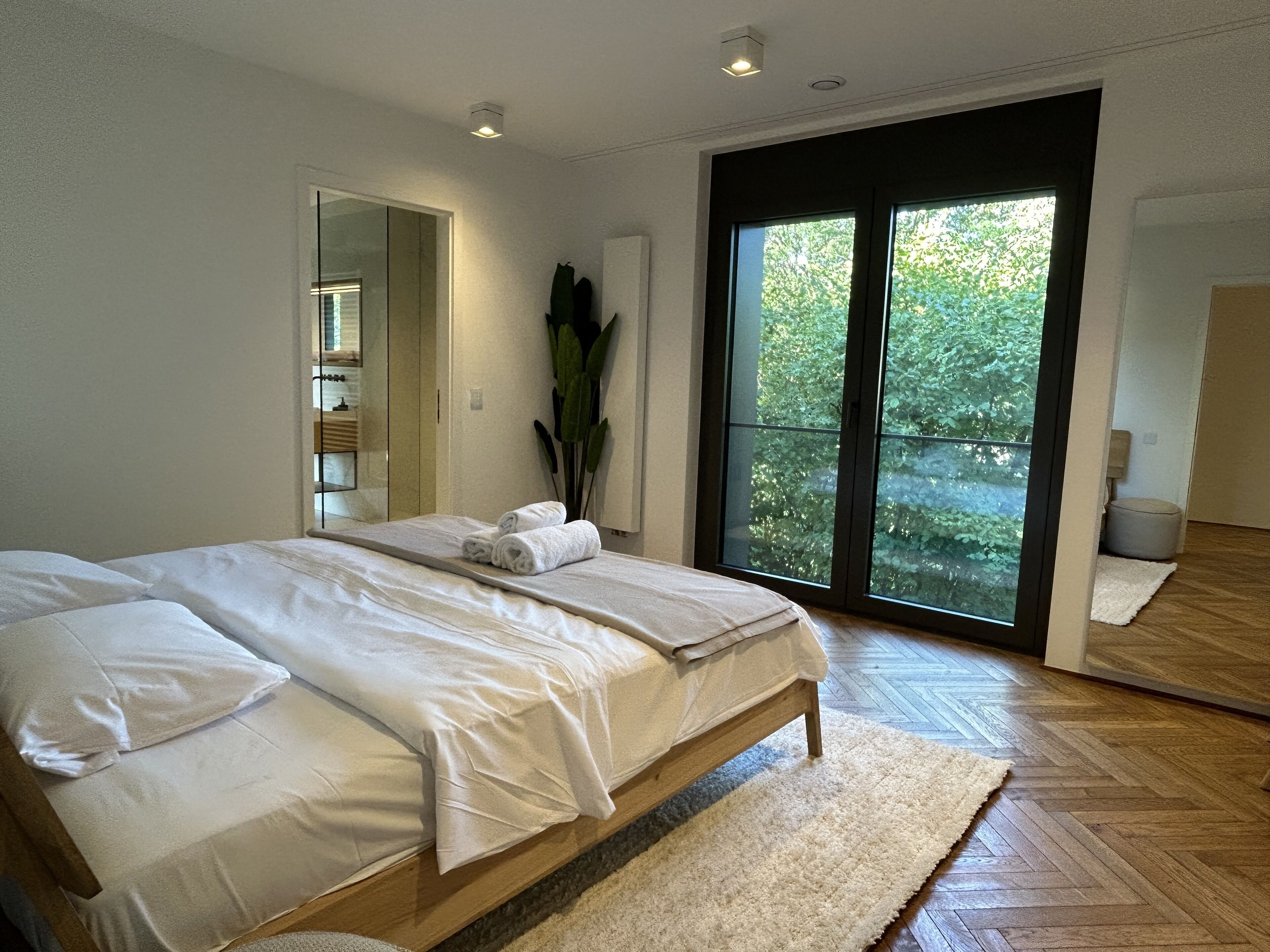 Ein modernes Schlafzimmer mit einem großen Bett, einer Schiebetür zum Balkon und einem Spiegel.