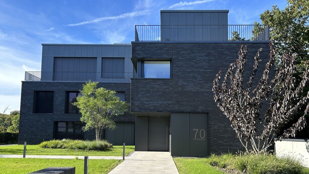 Een modern gebouw met een plat dak, grote ramen en een goed zichtbaar adresbord.