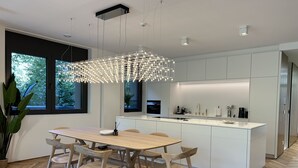Een moderne keuken met witte kasten, een houten eettafel en een bijzondere lamp.