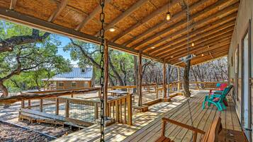 Relax on the covered deck surrounded by trees, featuring benches and chairs for a peaceful retreat.