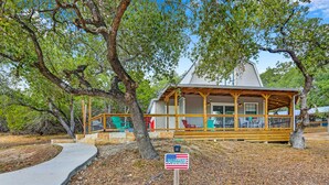 A covered outdoor seating area with a view of a building, surrounded by trees. - Charming Bulverde Farmhouse | Near San Antonio, Patio, BBQ, Hill Views (Bulverde)