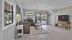 A spacious living room with a sofa, coffee table, and TV stand. - Charming Bulverde Farmhouse | Near San Antonio, Patio, BBQ, Hill Views (Bulverde)