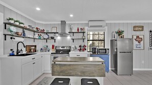 A modern kitchen with white cabinetry, a central island, stainless steel appliances, and decorative items on shelves. - Charming Bulverde Farmhouse | Near San Antonio, Patio, BBQ, Hill Views (Bulverde)