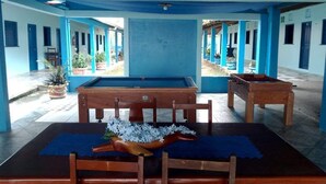 A pool table with a wooden table and chairs, surrounded by blue walls and columns. - My Stay  (Belo Horizonte)
