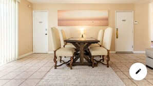 Een eethoek met een houten tafel en vier stoelen, een schilderij van een zonsondergang en twee deuren.