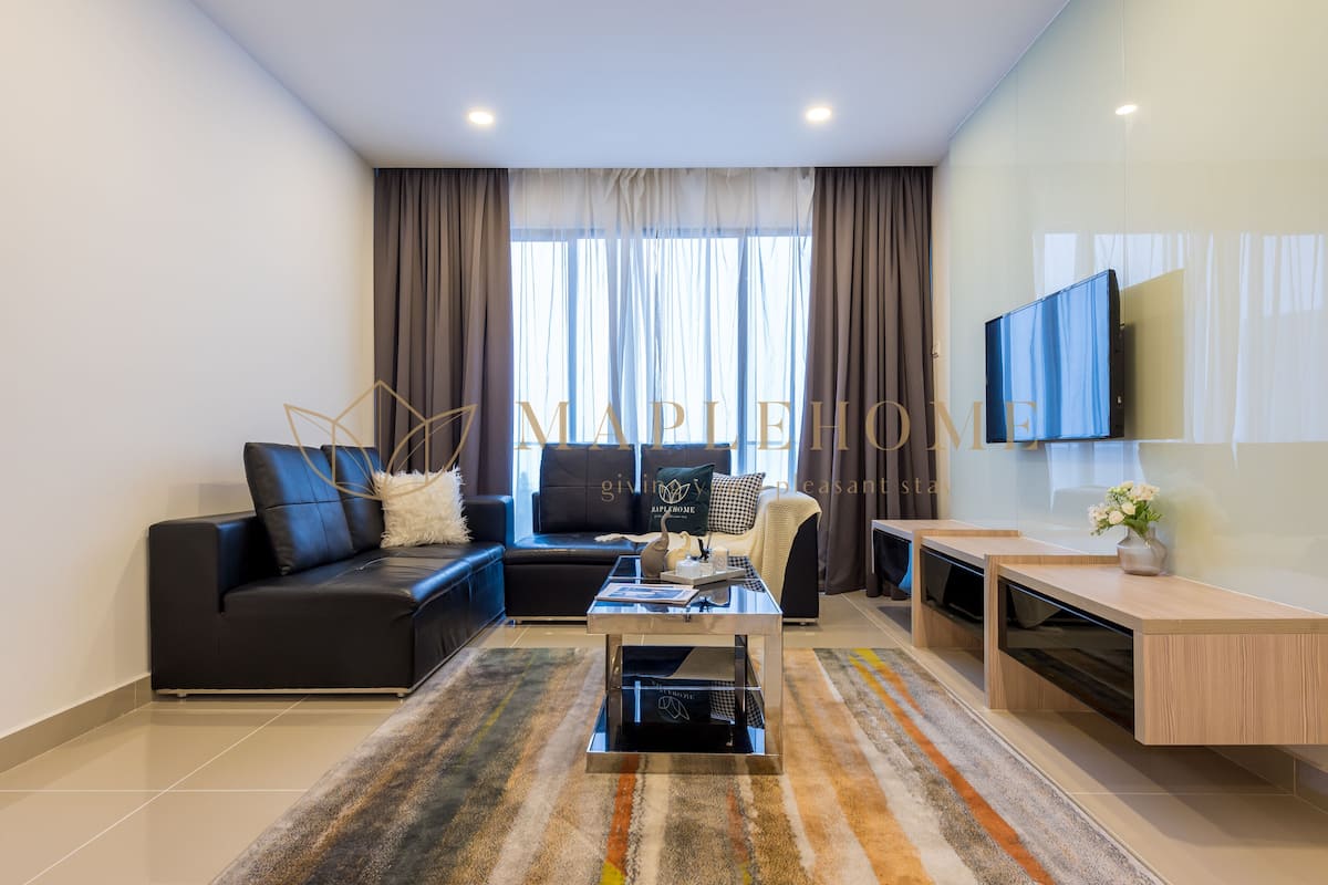A modern living room with a black sofa, a glass coffee table, and a TV mounted on the wall.