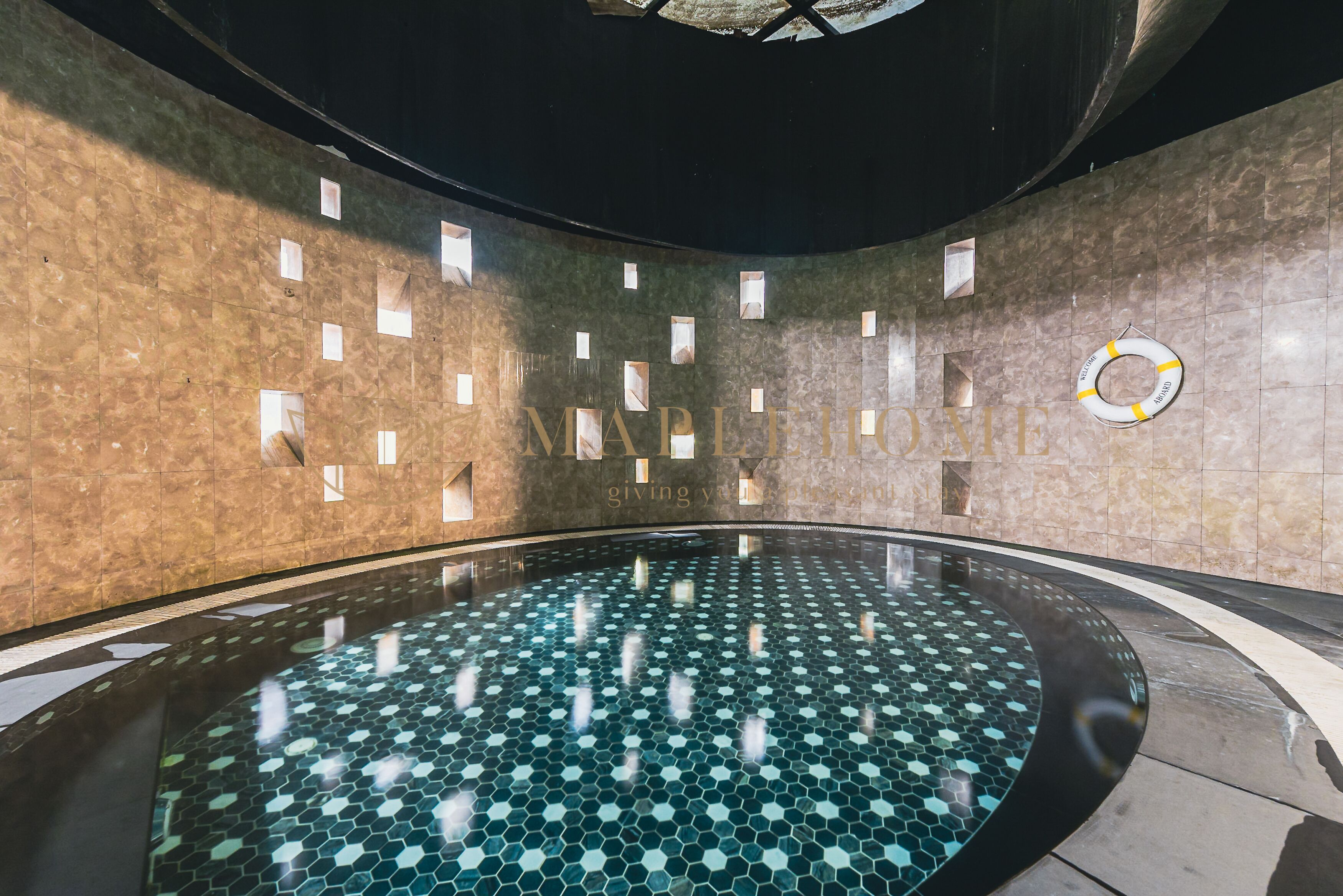 A modern indoor pool with a hexagonal tile pattern, recessed lighting, and a lifebuoy on the wall.