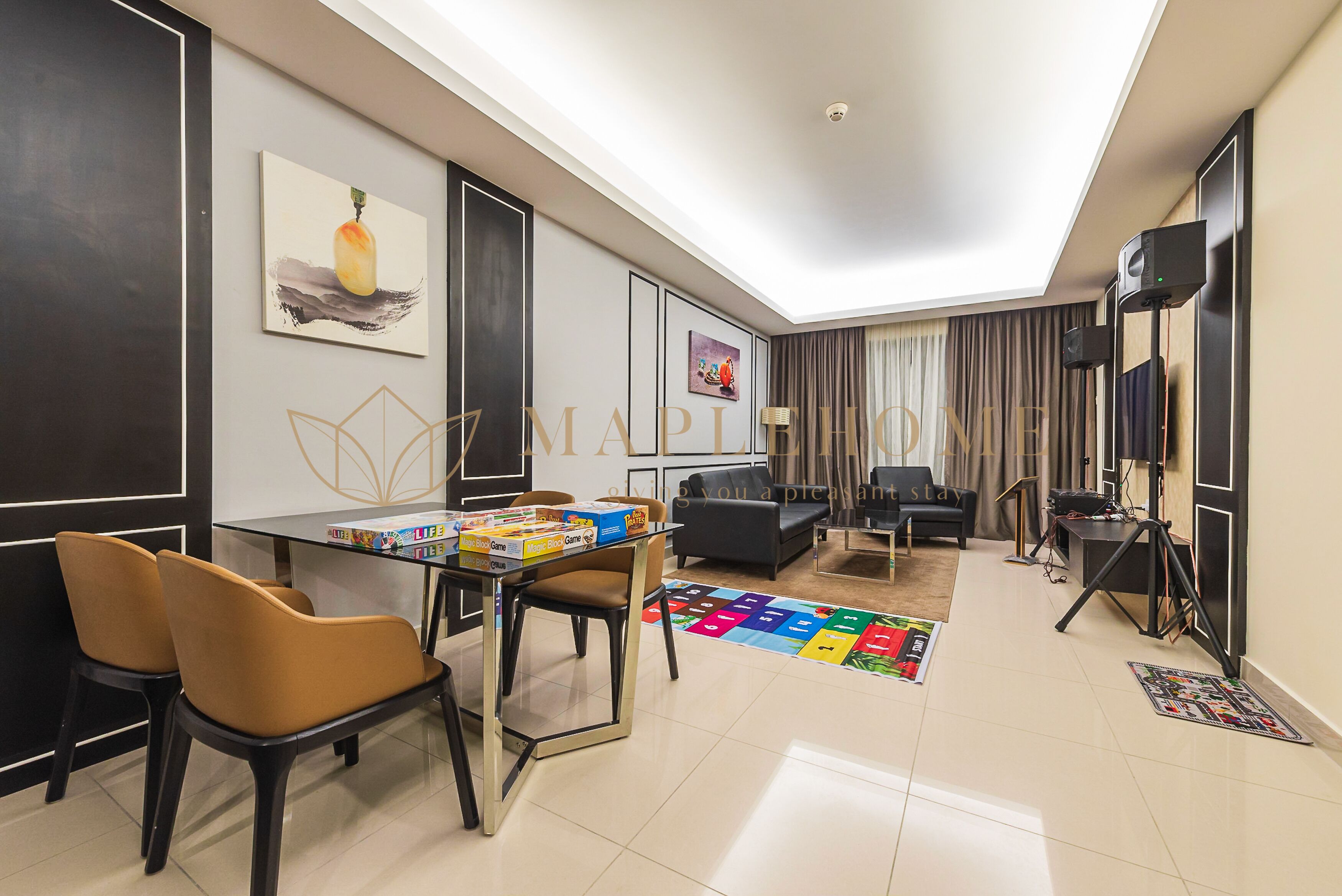 Una sala moderna con una mesa de vidrio, dos sillas marrones, un sofá negro, una alfombra colorida y un televisor de pantalla plana montado en la pared.