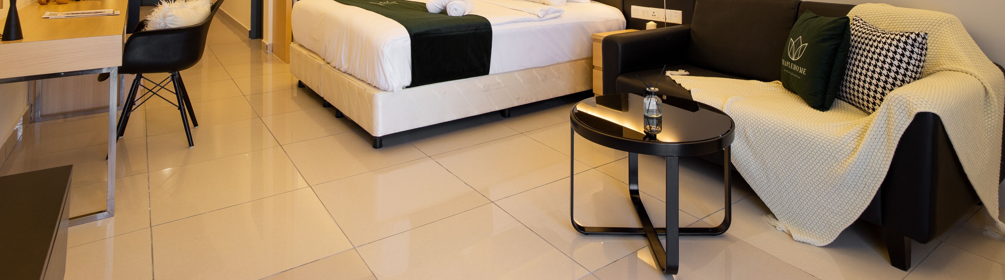 A hotel room with a bed, a round table with a lamp, a chair, and a sofa.