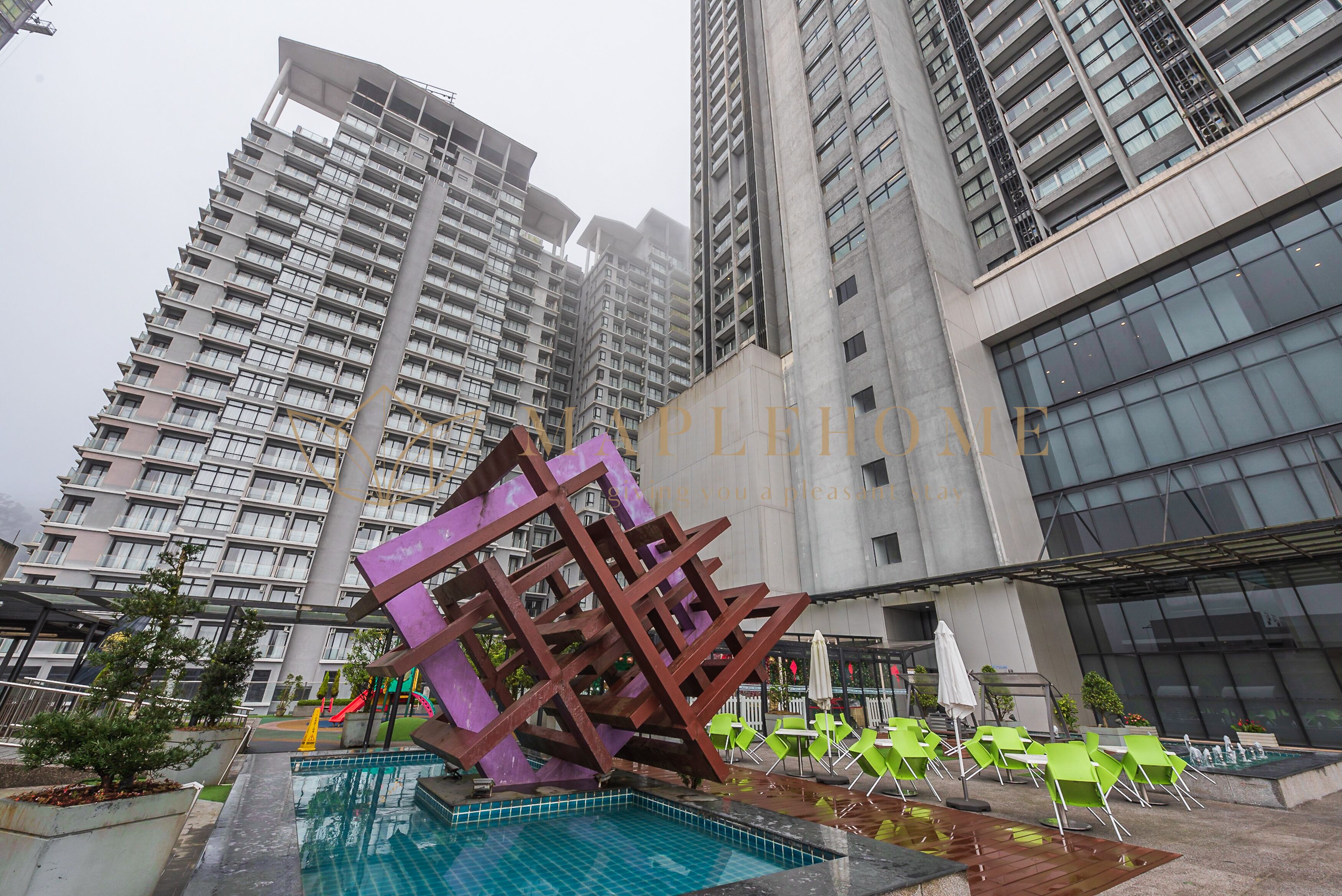 Un edificio moderno con área de piscina, que incluye una escultura metálica única, sillas verdes y un tobogán.