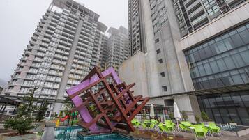 Un edificio moderno con área de piscina, que incluye una escultura metálica única, sillas verdes y un tobogán.