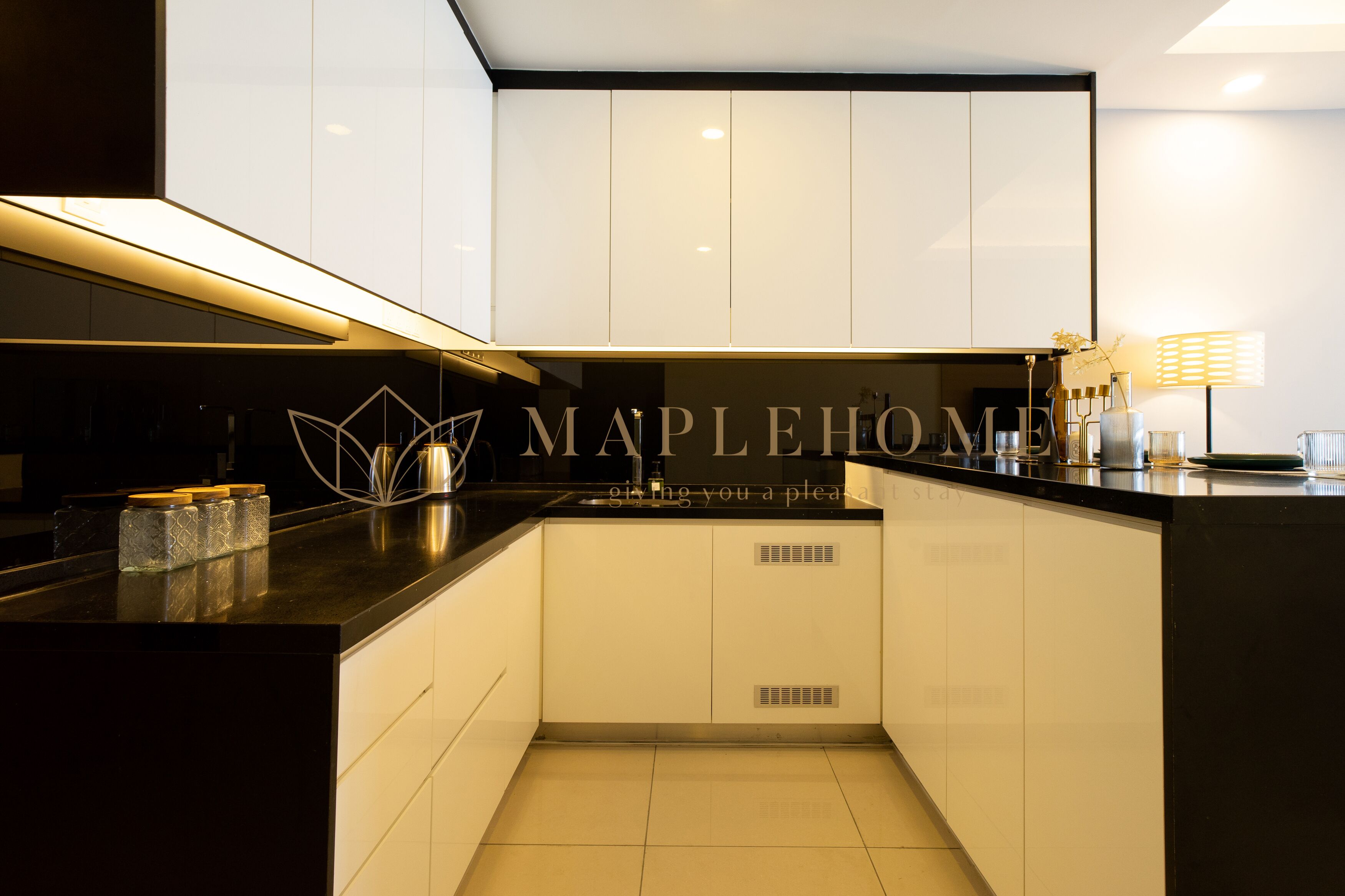 A modern kitchen with white cabinets, a black countertop, and a logo that reads "MAPLEHOME".