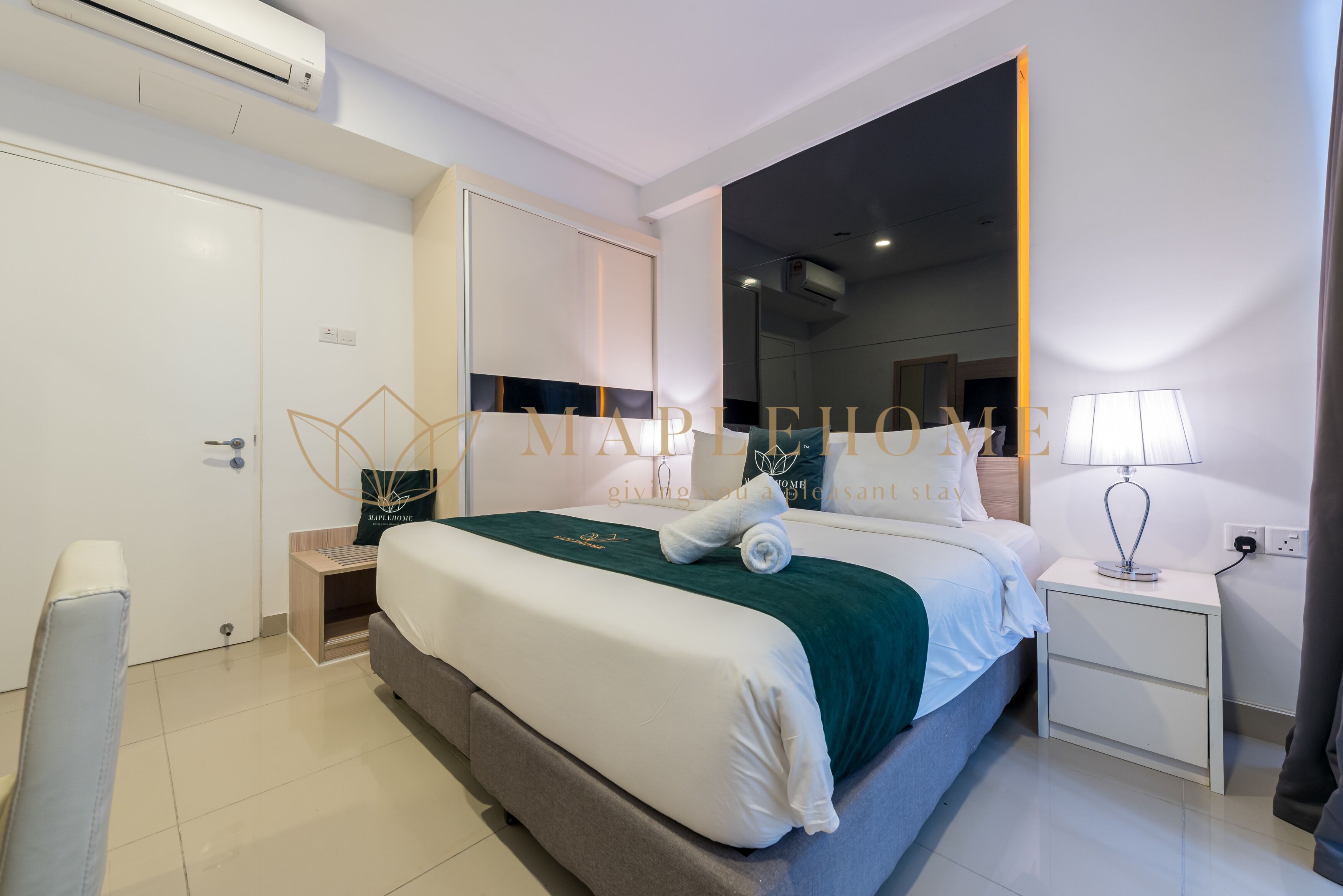 A modern hotel room with a large bed, a bedside table with a lamp, a wardrobe, and a mirror.