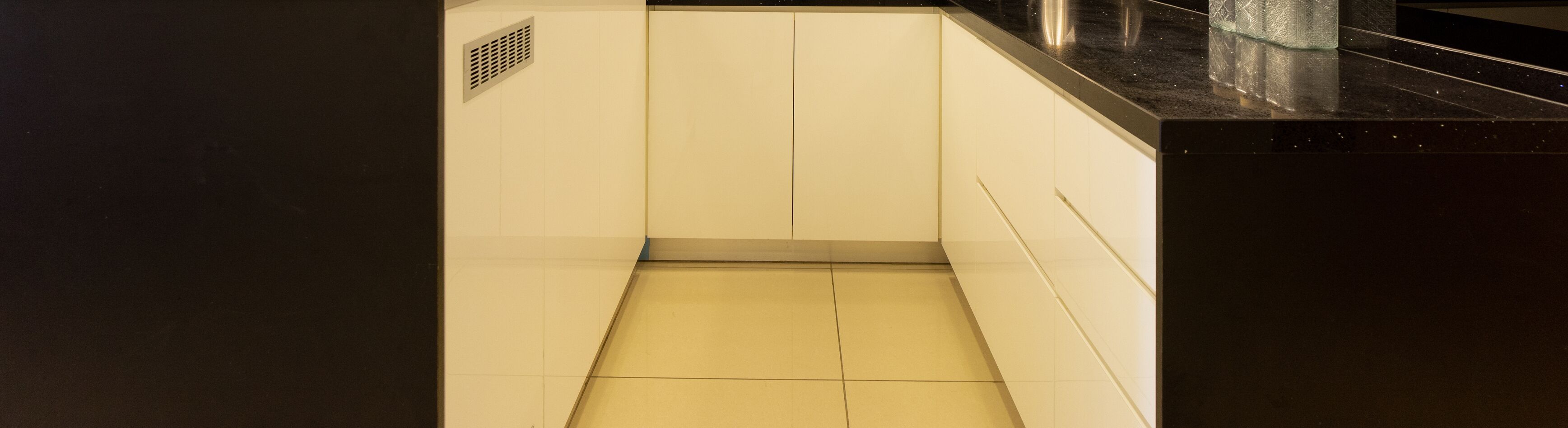 A narrow, tiled bathroom with a black countertop and a vent on the wall.