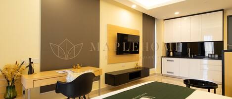 A modern hotel room with a bed, a desk, a chair, a TV, a kitchen area, and a bathroom.