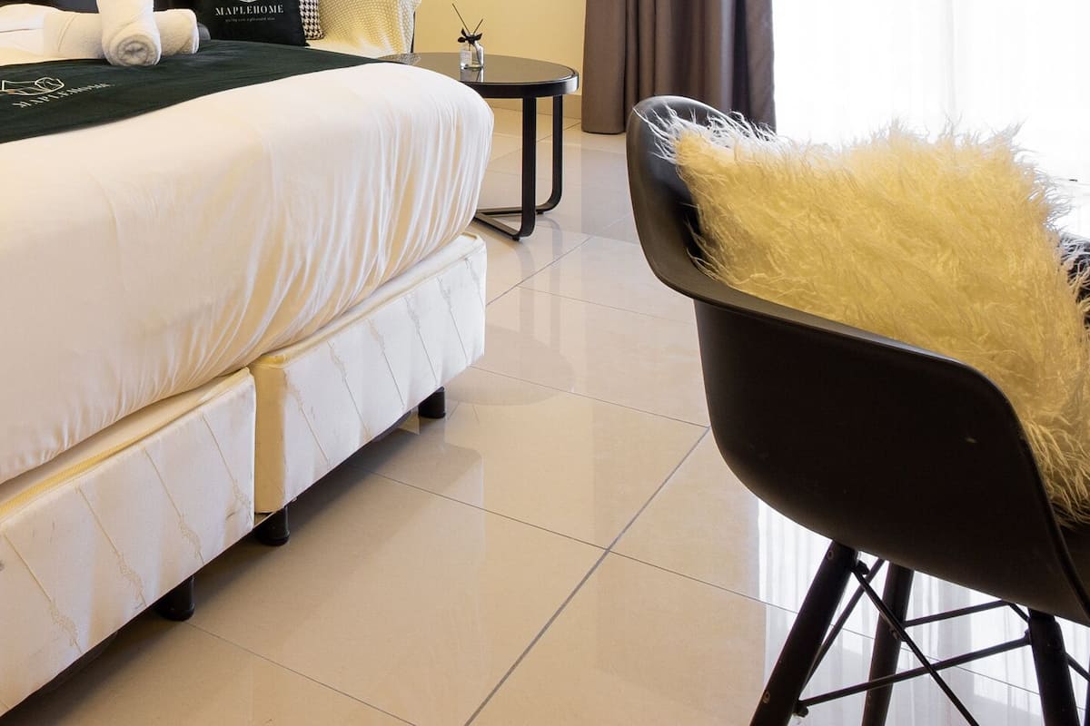 A hotel room with a bed, a bedside table, a chair, and a small table with a lamp.