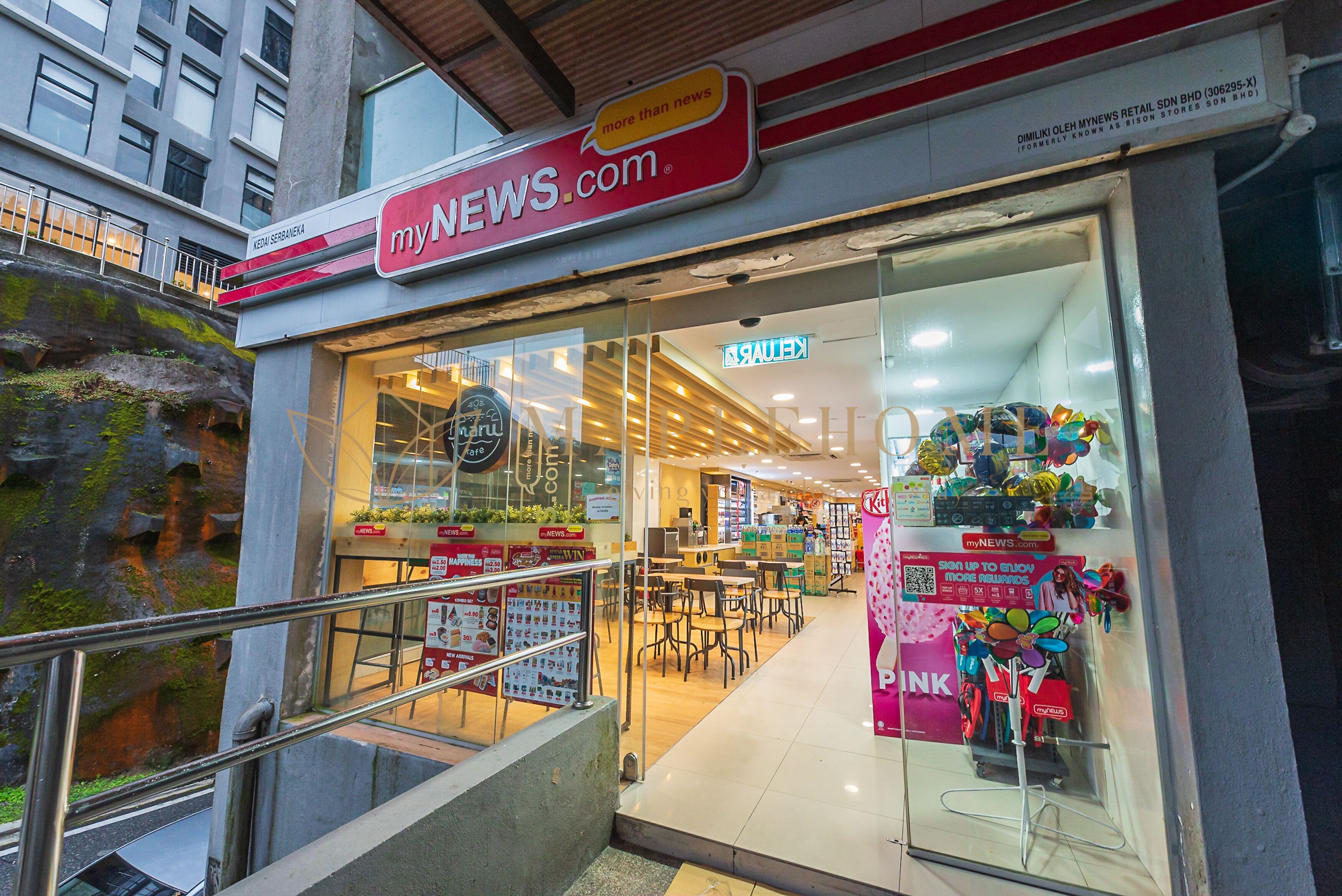 A newsstand with a glass entrance, a staircase, and a view of the interior with tables and chairs.
