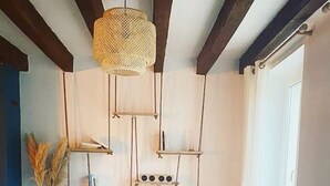Una habitación con piso de madera, una silla de mimbre, una mesita y un mueble de pared con libros y objetos decorativos.