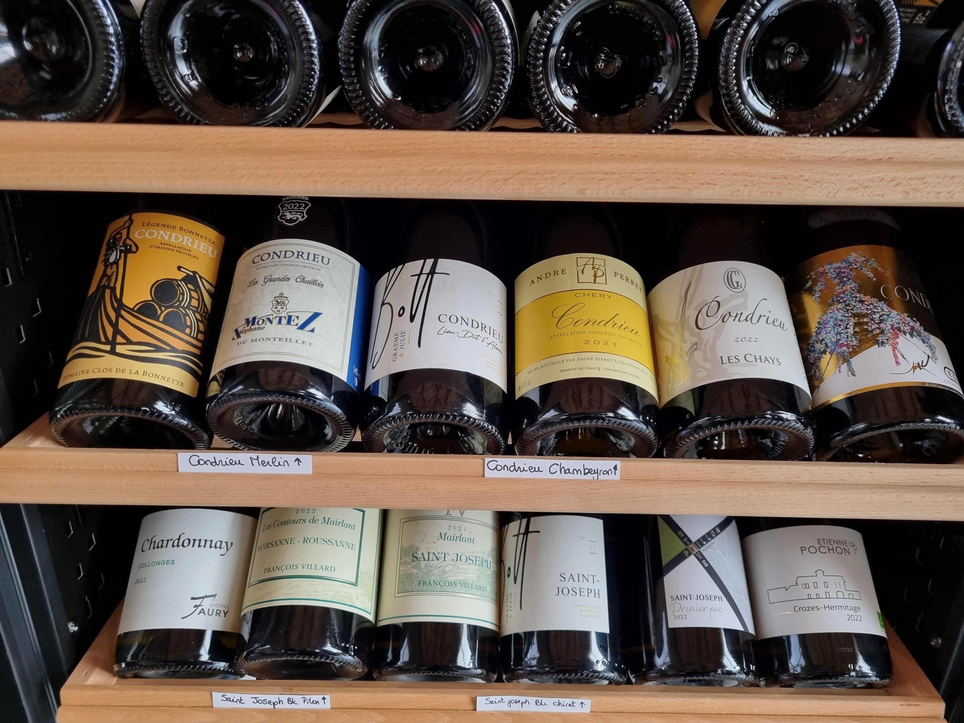 Una dispensa per vino con bottiglie etichettate 'Condrieu' e 'Saint Joseph'.