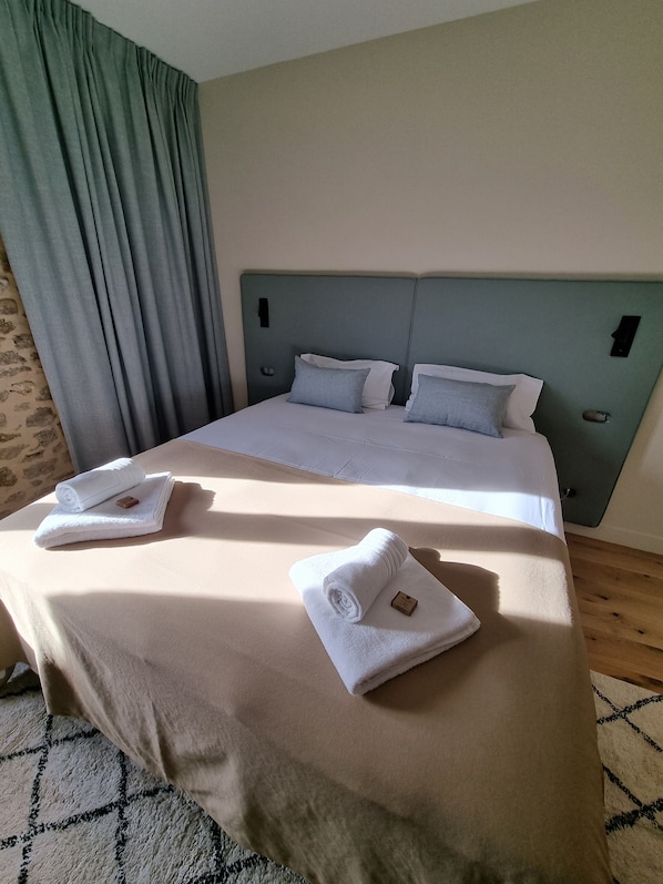 Una cama bien hecha con sábanas blancas y dos toallas enrolladas sobre la cama.