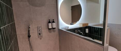 A modern bathroom with a shower, a toilet, and a large mirror with a circular light.