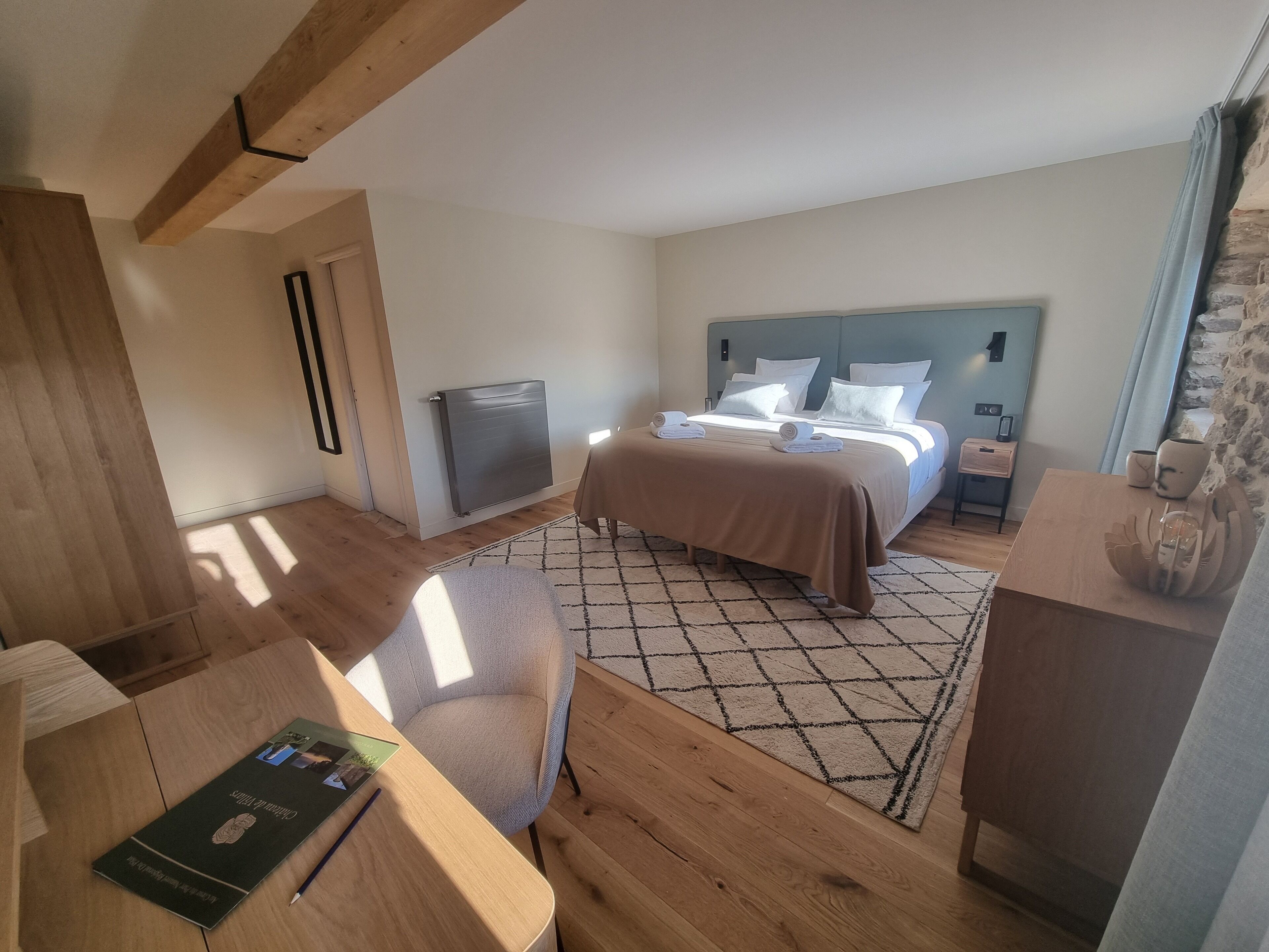 Una habitación de hotel con cama, escritorio, silla, mesita pequeña y radiador.