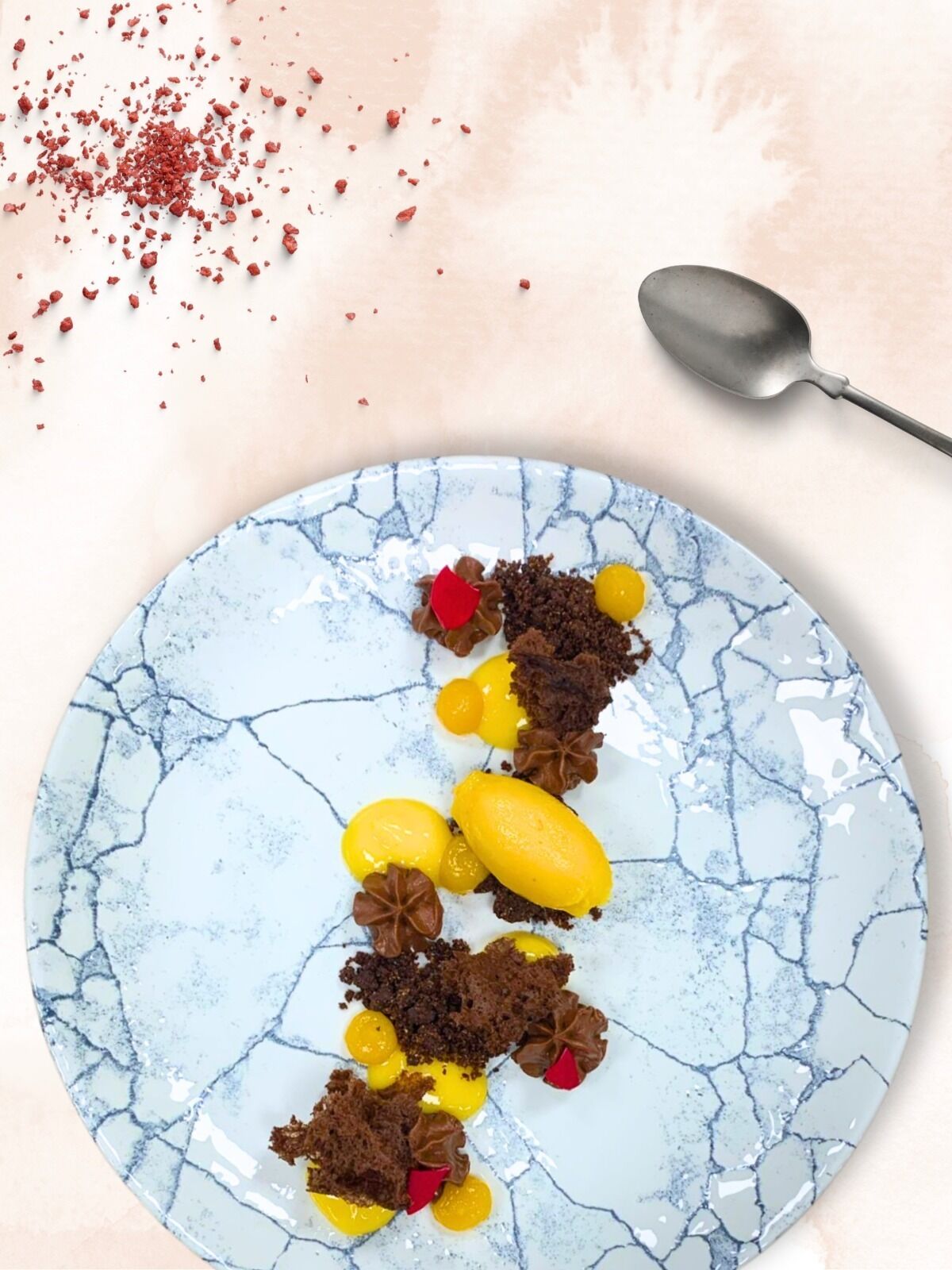 A dessert on a plate with a cracked blue pattern, a spoon, and scattered red crumbs.
