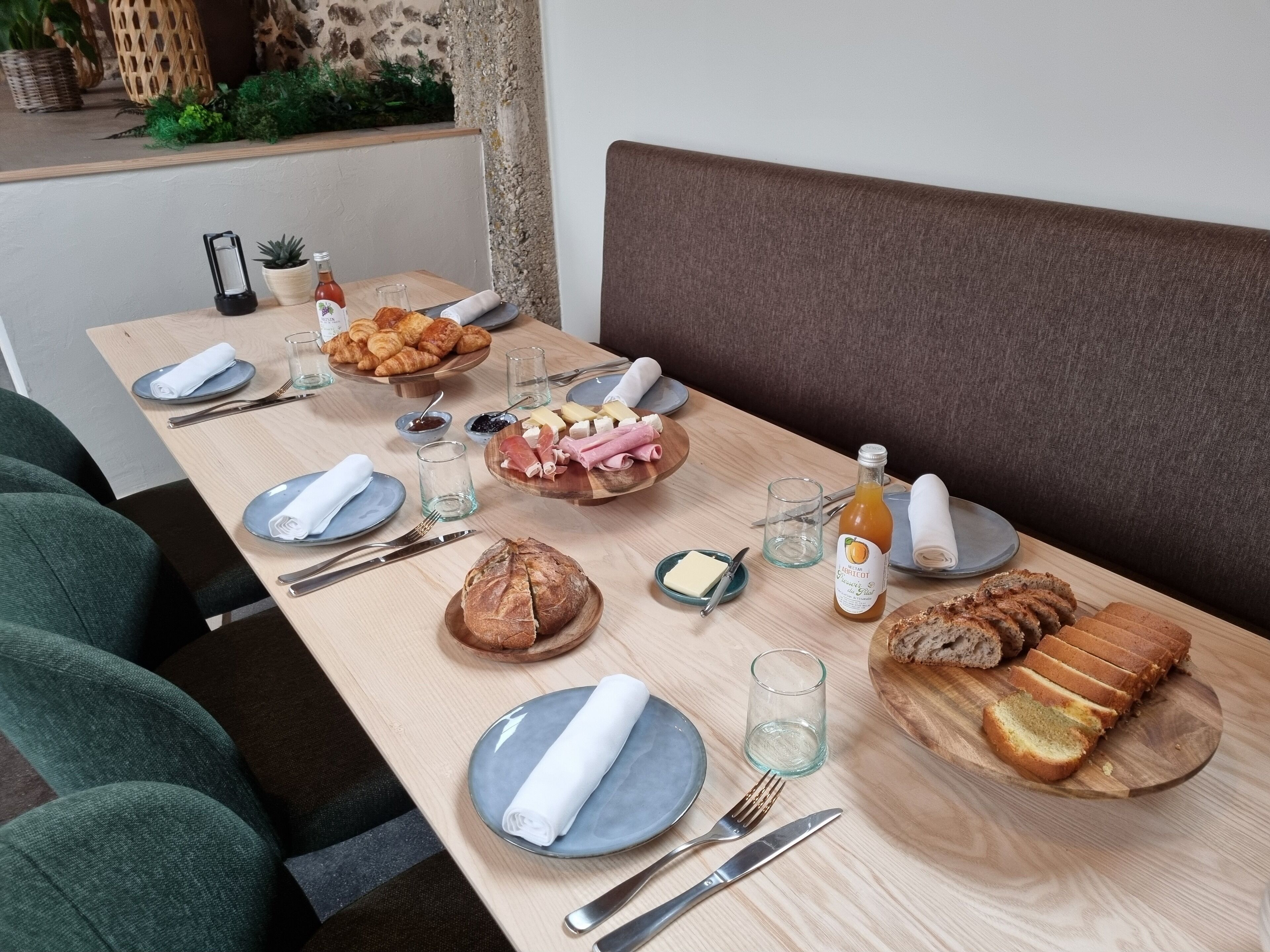 A breakfast table set with croissants, cheese, ham, bread, and a bottle of juice.