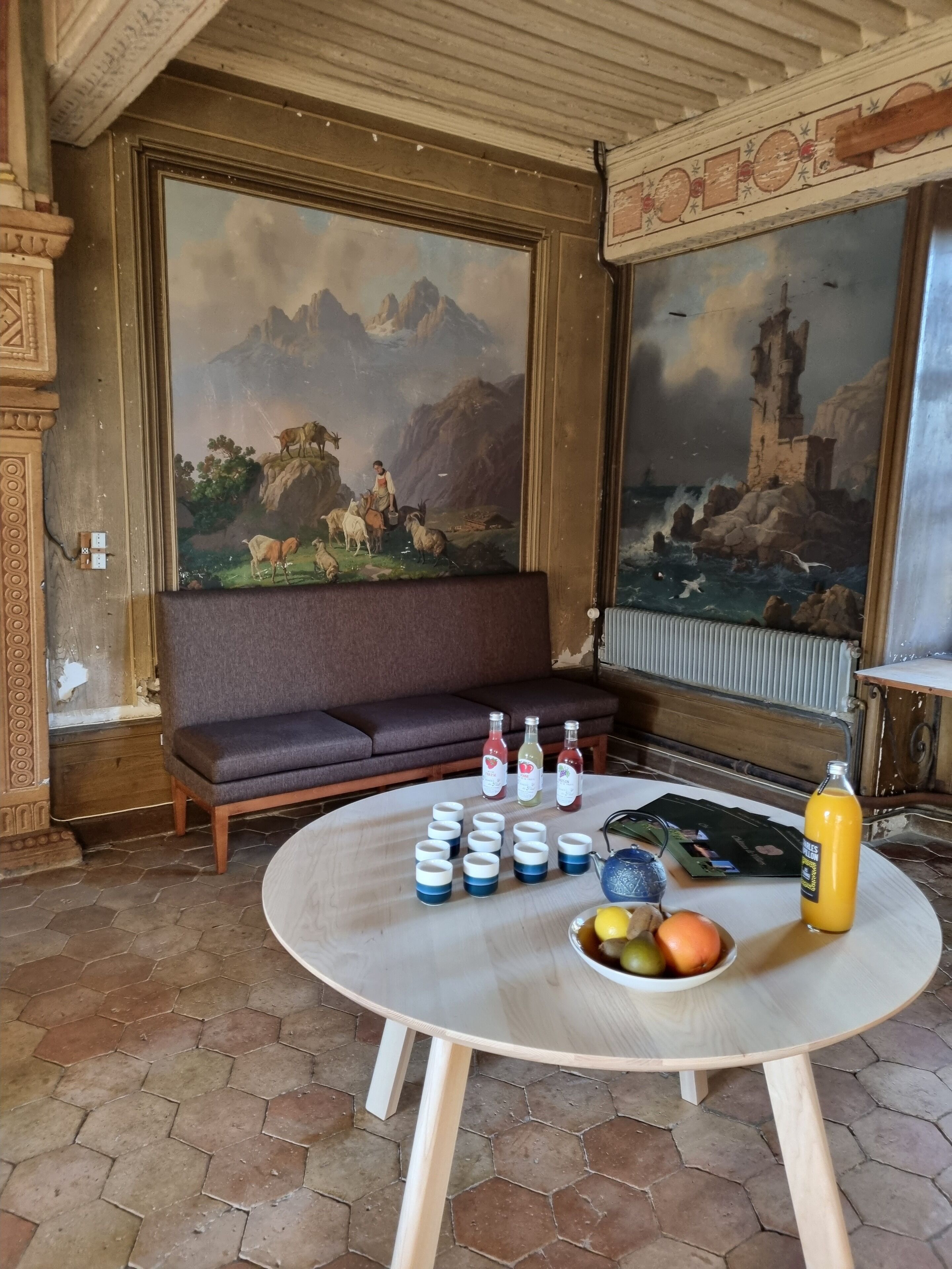 A room with a round table, a sofa, and two large paintings on the walls.