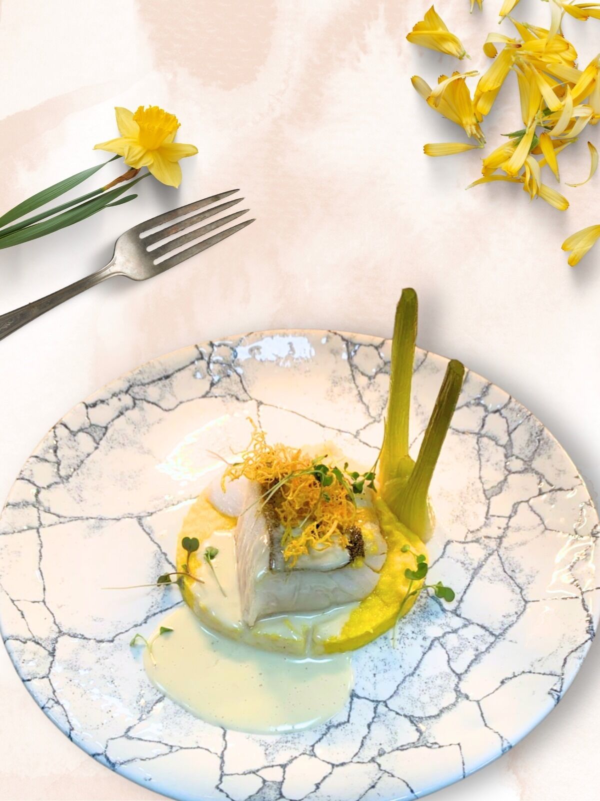 A dish with a creamy sauce, garnished with green herbs and shredded topping, on a cracked white plate.