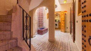 A hallway with a staircase, patterned floor, and a view into a room with a washing machine. - Riad Colette Exclusif - Médina - Petit déjeuner - Wifi (Marrakech)