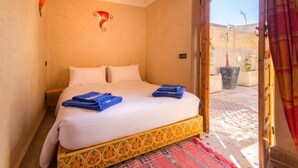 A hotel room with a bed, two pillows, a decorative wall piece, a nightstand, and a view of the outside. - Riad Colette Exclusif - Médina - Petit déjeuner - Wifi (Marrakech)