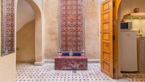 A hallway with a tiled floor, a decorative wall panel, and a wooden door leading to a kitchen area. - Riad Colette Exclusif - Médina - Petit déjeuner - Wifi (Marrakech)